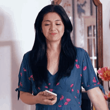 a woman in a blue dress with pink flowers is looking at her phone