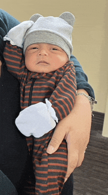 a woman is holding a baby wearing a striped outfit and a bear hat