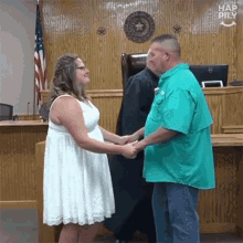 a man in a green shirt and a woman in a white dress are holding hands in front of a judge .