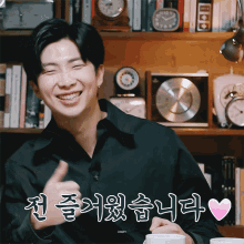 a man in a black shirt is smiling and giving a thumbs up in front of a bookshelf with clocks on it