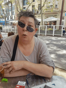 a woman wearing sunglasses sits at a table with a pack of mata fumar cigarettes in front of her