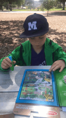 a young boy wearing a hat with the letter m on it is playing with a water reveal pad