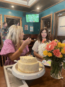 two women sitting at a table with a cake and flowers