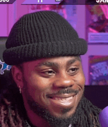 a man with dreadlocks and a beard wearing a black beanie is smiling .