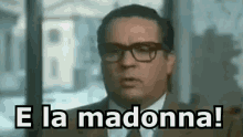 a man wearing glasses and a suit is saying `` e la madonna ! ''