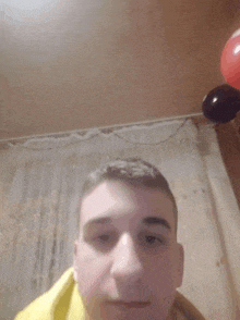 a man in a yellow shirt is taking a selfie in a room with balloons in the background .