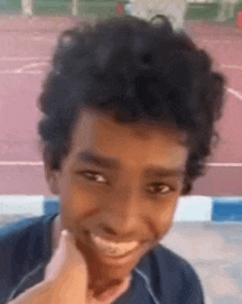 a young boy with curly hair is smiling and touching his face with his hand .