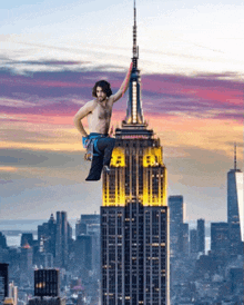 a shirtless man is sitting on the top of the empire state building