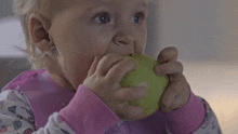 a little girl is eating a green apple while wearing a pink sweater .