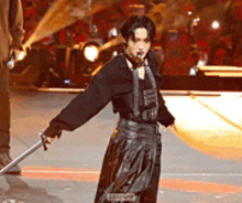 a man is holding a sword on a stage while wearing a black outfit .