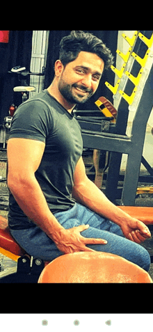 a man with a beard is sitting on a bench in a gym smiling .