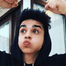 a young man wearing a black hoodie is making a funny face with his hands .