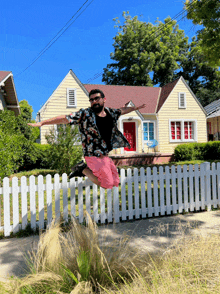 a man jumps over a white picket fence in front of a yellow house