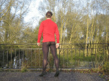 a man in a red shirt and black tights is standing on a bridge