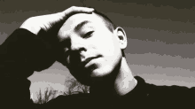 a black and white photo of a young man touching his head