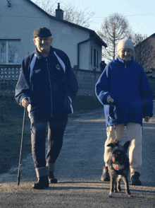 a man wearing a reebok jacket walks with a woman walking a dog