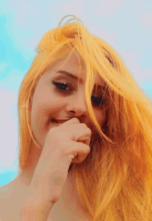 a woman with bright yellow hair is smiling and covering her mouth with her hand