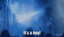 a crowd of people standing in front of a waterfall with the words `` it 's a boy '' written on the screen .