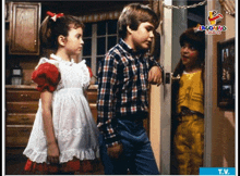 three children are standing in front of a door that says t.v. in the corner