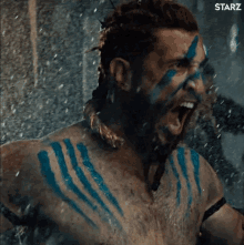 a man with blue paint on his face and chest is screaming