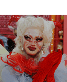 a drag queen with white hair and red horns looks at the camera