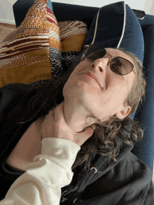 a man wearing sunglasses is laying on a couch with a person holding his neck