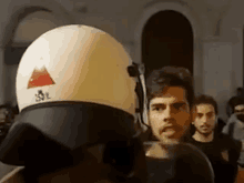 a man wearing a helmet and headphones is talking to another man in a crowd .