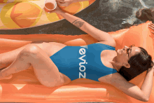 a woman in a blue evioz swimsuit is laying on an orange raft