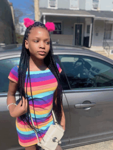 a young girl wearing a rainbow striped dress stands in front of a car