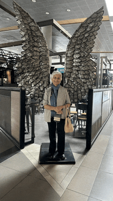 an older woman stands in front of a large angel statue