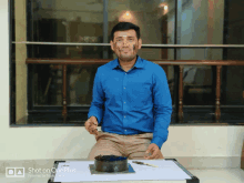 a man in a blue shirt is sitting at a table with a cake on it and a shot on oneplus