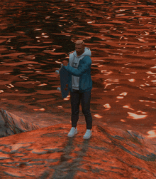 a man holding a skateboard in front of a body of water with the word cat on his sweatshirt