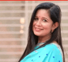 a woman in a blue saree is smiling for the camera and looking at the camera .