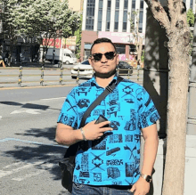 a man wearing sunglasses and a blue shirt stands in front of a street