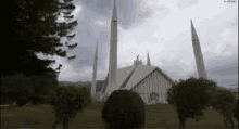 a mosque with a lot of trees in front of it and a cloudy sky in the background .