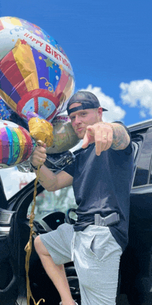 a man in a black shirt is pointing at a happy birthday balloon