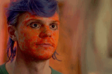 a man with blue hair and red paint on his face looks at the camera