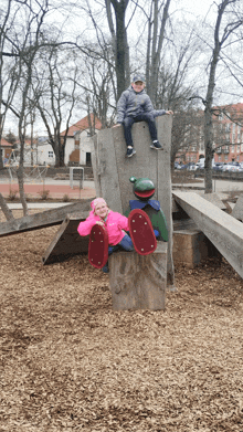 a boy and a girl are sitting on a wooden structure in a park