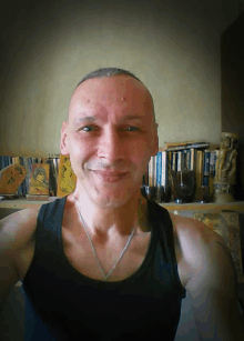 a man wearing a black tank top is smiling in front of a shelf full of books