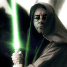 a woman in a hooded robe is holding a green light saber