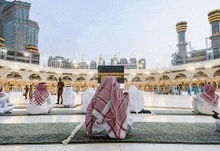 a group of men are sitting on a carpet in front of a mosque .