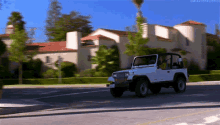 a white jeep is driving down a street in front of a large white house