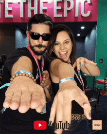 a man and a woman are posing for a picture in front of a sign that says te the epic