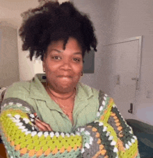 a woman with curly hair is standing in a room with her arms crossed and making a funny face .