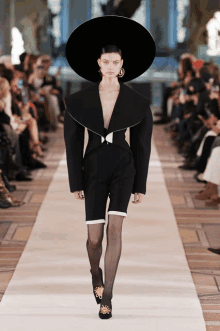 a model walks down the runway at a fashion show wearing a black hat