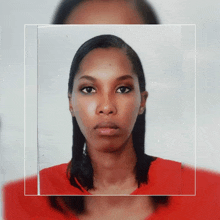 a woman in a red shirt looks at the camera with a serious look on her face