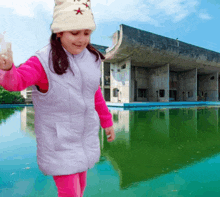 a little girl wearing a white hat and a purple vest stands in front of a building