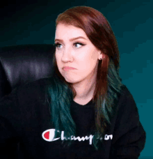 a woman with green hair is wearing a black champion sweater