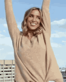 a woman wearing a tan sweater is standing with her arms in the air .