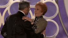 a man in a tuxedo is hugging a woman in front of a nbc logo